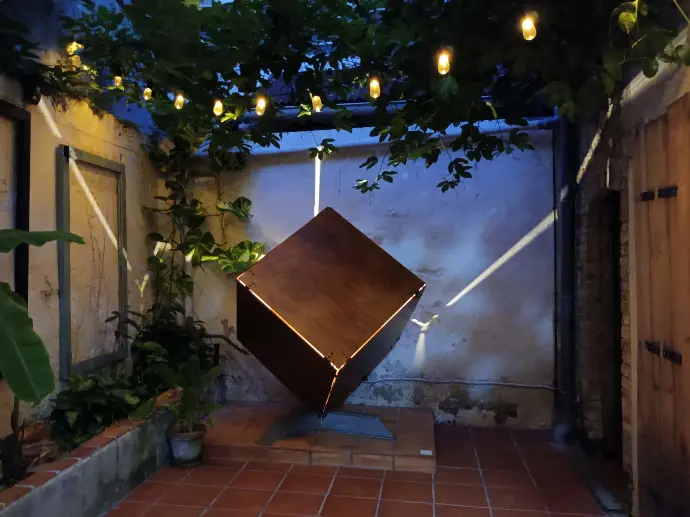 Installation artistique d'un cube éclairé de l'intérieur dans un patio.